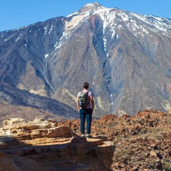 Back view of traveler man standing on the edge of rock looking to volcano El Teide in National park of Tenerife, Canary Islands, Spain. Travel the world